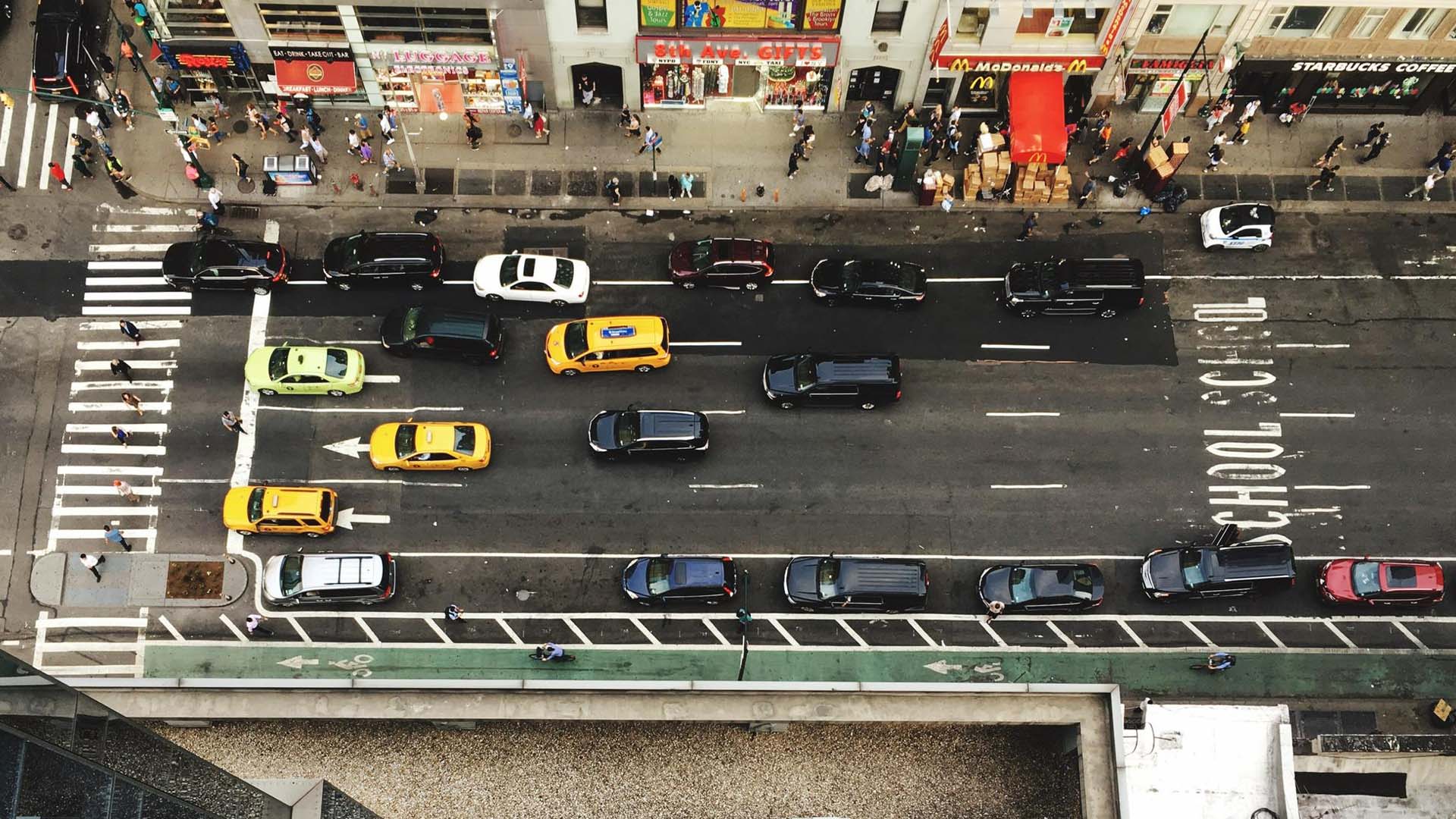 Cars driving on a busy New York City street with a banner highlighting Alternate-Side Parking rules and fines